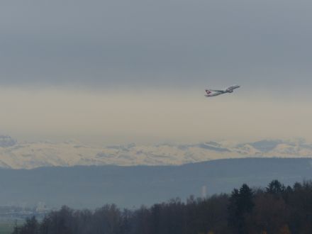 Abfliegendes Flugzeug vor Bergen in trübem Licht.