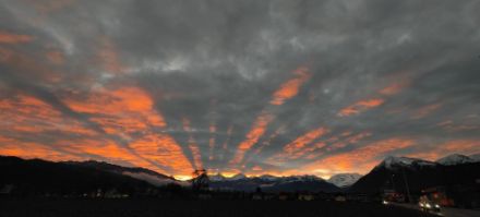 Sonnenaufgang bei Thun. Sonnenstrahlen erleuchten die Unterseite der hohen Bewölkung orange.