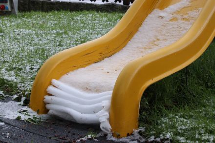 Eine dünne Schicht nassen, schweren Schnees liegt auf einer Rutsche und faltet sich zusammen. Solche Anblicke gibt es oft im Frühling.