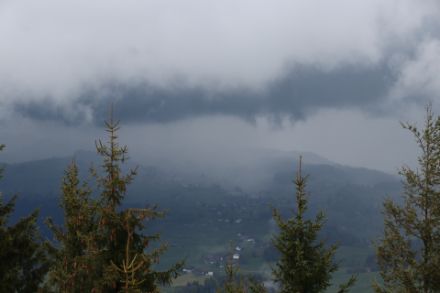 Dunkelgraue, tiefe Wolken über Hügeln und Nadelbäumen.