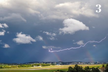 Ein primärer- und ein sekundärer Regenbogen mit einem Blitz vor dem dunklen Himmel, Flughafen Zürich.