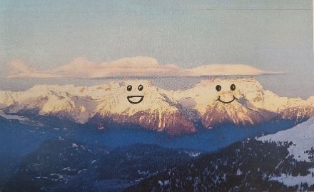 Blick zu den genannten Bergen. Auf das Webcambild sind zwei Smileys gemalt, wodurch die Berge zusammen mit der Altocumulus-Bewölkung knapp über den Gipfeln wie Gesichter aussehen.