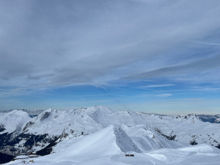 Aussicht auf Berge, darüber ausgedehnte Wolkenfelder, im Hintergrund blauer Himmel.