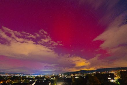 Rotes Nordlicht am Nachthimmel über den Lichtern der Stadt Winterthur.