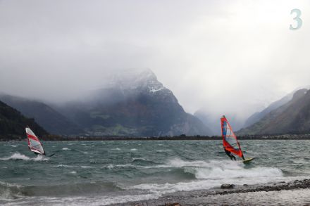 See mit Wellengang, Windsurfern und Wolken.