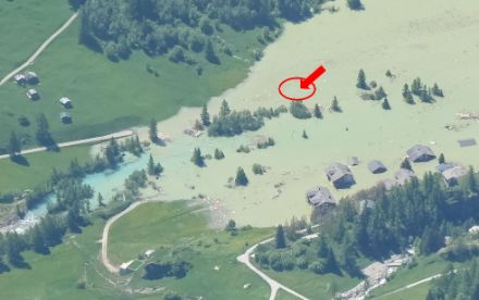Das Gebiet der aufgestauten Lonza in Blatten am 30. Mai 2025. An der rot markierten Stelle befand sich die Wetterstation Blatten. Ganz knapp und unscharf ist noch der herausragende Windmessmast erkennbar (roter Pfeil)