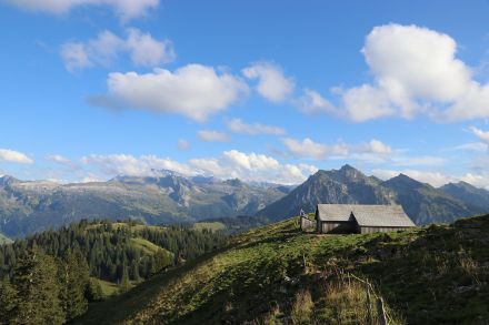 Eine Alphütte in den Bergen, darüber ein tiefblauer Himmel mit einigen Quellwolken.
