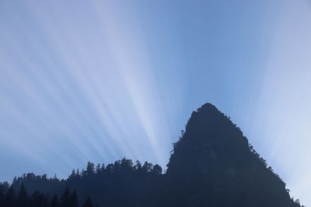 Schattenstrahlen, die fächerartig hinter einem Berg hervortreten und nach oben strahlen.