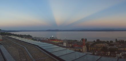 Blick über einen See, darüber breiten sich Gegendämmerungsstrahlen aus, die am Horizont verschwinden.