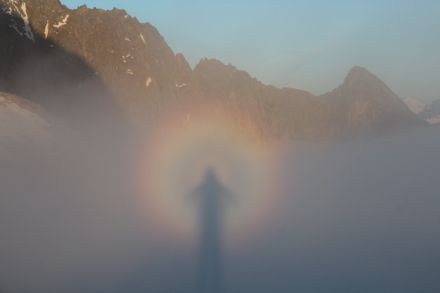 Aufnahme einer Berglandschaft, im Nebel im Vordergrund sind farbige Kreise und der Schatten des Beobachters zu sehen.