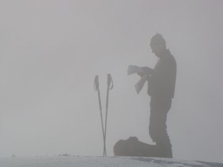 Bild eines Skitourenfahrers im Nebel, der eine Karte konsultiert.