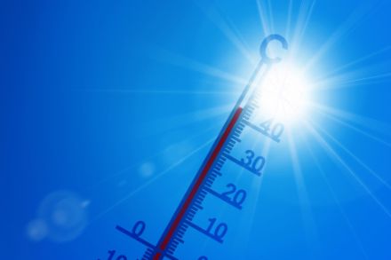 Klassisches Thermometer mit hohen Temperaturen vor blauem Himmel und Sonne