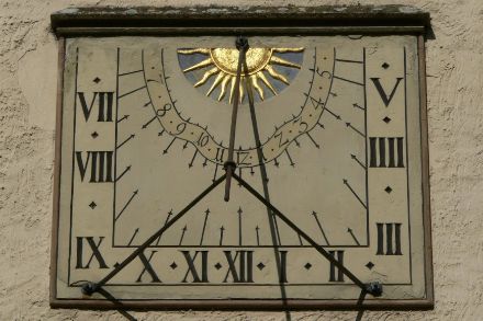 Vertikale Sonnenuhr mit Polstab an einer nach Süden gerichteten Wand, der Stabschatten dreht gegen den Uhrzeigersinn. Quelle: https://de.wikipedia.org/wiki/Sonnenuhr