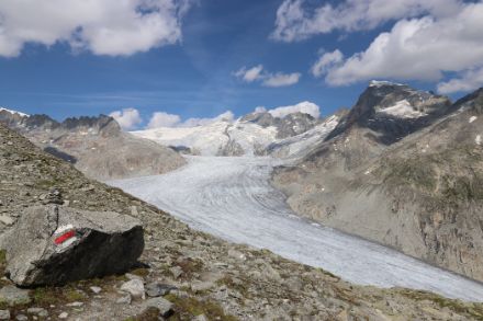 Foto des Rohnegletschers bei leichter Bewölkung. Im Vordergrund ist ein Wanderwegzeichen zu sehen.