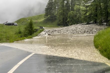 Eine Bergstrasse ist nach starken Regenfällen überflutet, das Wasser bedeckt die Fahrbahn und macht sie unpassierbar.